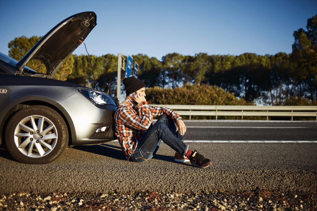 young brutal man sits near car talking on cell phone because his